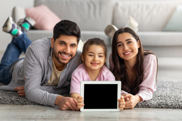 Happy family of eastern parents and little girl showing digital tablet with empty screen for mockup