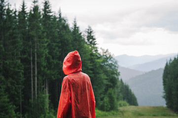 Person in a red raincoat stands on the rain in the mountains against backdrop of a beautiful landscape with coniferous trees and fog. Hiker in the Carpathian Mountains in the Rain. Copy space