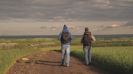 Travelers with backpacks are walking along road. Teamwork. Hikers travel along a country road and admire beautiful landscape. Adventure and travel concept. Tourists enjoy relaxation and nature