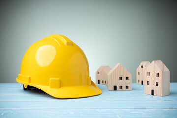 Yellow hard hat with many mini wood houses on blue wooden table with copy space and green background. Concept construction home, and safety on work. Personal protective equipment.