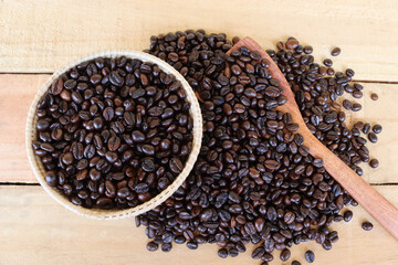 Coffee beans in the wicker basket and wooden spoon isolated on wooden background closeup.