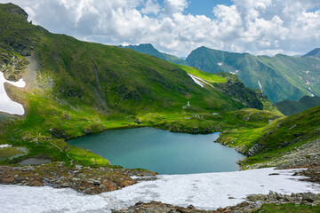 Fototapeta na wymiar capra lake of fagaras mountains. wonderful summer nature scenery on a sunny day. popular travel destination of romania. snow and grass on the slopes. fluffy clouds on the sky