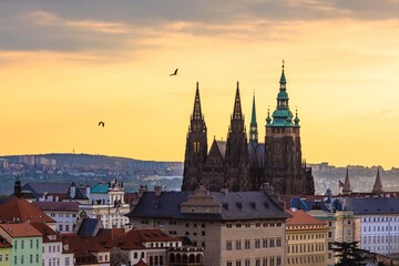 Obraz premium Prague, Czech Republic - May 3 2021: View of the Prague castle during morning sunrise. Orange and blue sky in the background and two birds flying by.