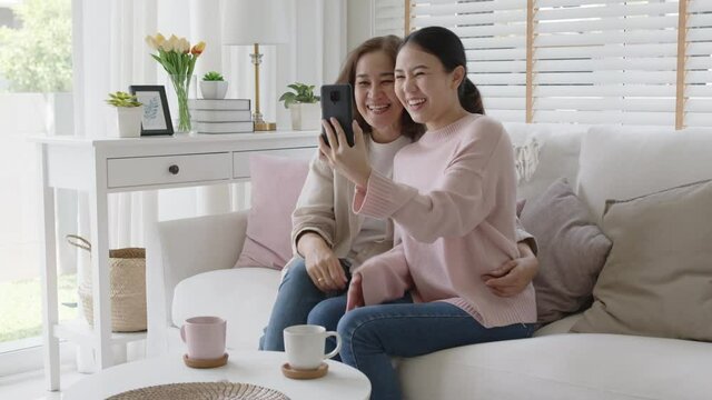 Retired healthy mom and girl two people hold phone waving hand greeting selfie look at camera on webcam app at relax comfort sofa couch living room in health care quarantine social distance isolate.