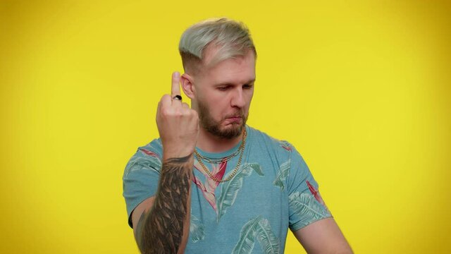 Aggressive crazy hooligan stylish tourist guy showing around his middle fingers, demonstrating protest with impolite rude gesture of disrespect, rejecting communication. Young man on yellow background