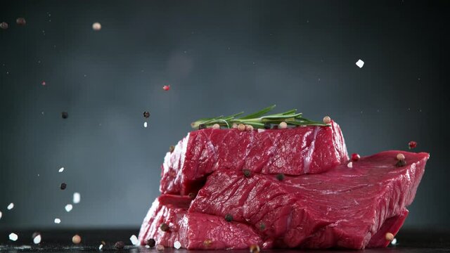Flying pieces of raw beef steaks falling on table with spice. Filmed on high speed cinema camera, 1000 fps.