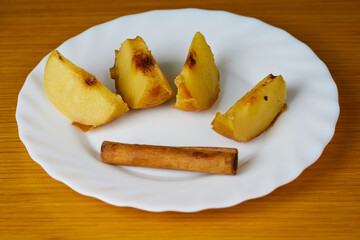 Tasty Baked Apple slices decorated with cinnamon sticks on a plate and wooden background