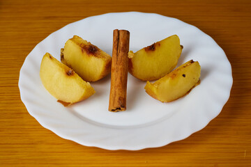 Tasty Baked Apple slices decorated with cinnamon sticks on a plate and wooden background