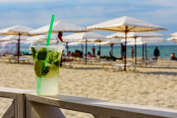 Mojito cocktail on wooden table with sandy beach on a background