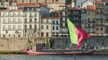 Porto, Portugal. A small riverside town with tiled buildings as seen from a bank. Close-up of the Portuguese national flag with traditional boat in the background. High quality 4k footage - Powered by Adobe
