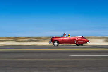 Fototapeta na wymiar A red classic car driving along the Malecon in Havana, Cuba.