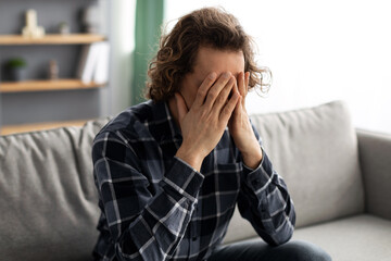 Unhappy Guy Covering Face Suffering From Depression Sitting At Home