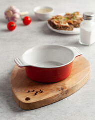 An empty red bowl on a wooden chopping board for soup, slices of bread with salted pork bacon or lard