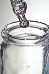 Cosmetic pipette with drops of transparent liquid and a jar, close-up on a colored background.