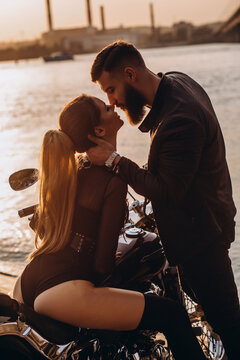 Evening walk of a biker and a girl on the river bank. Photoshoot at sunset.