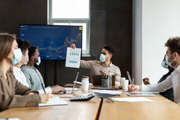 Man in protective medical mask showing paper with graph diagram