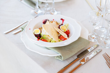 Salad with stewed boiled beef and cranberry sauce on a served plate on the table. Slices and halves of cherry tomatoes and a bread cake. Splashes of red sauce on a plate.