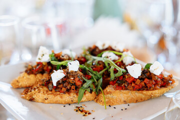 Italian appetizer on white slate background. Crusty bruschetta with concasse tomatoes, stracciatella cheese decorated with rucola. Delicious and healthy restaurant meals, copy space, closeup