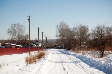 Winter road through the village, track in the snow, snowdrifts.