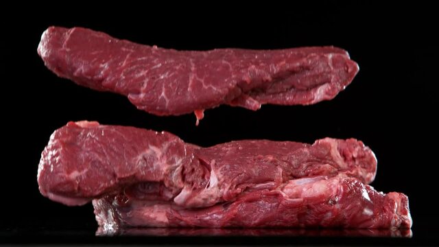 Flying pieces of raw beef steaks falling on table. Filmed on high speed cinema camera, 1000 fps.