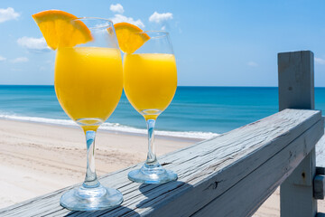 Two glasses with mimosa cocktail. Yellow drink with bubbles glows in the sun on the background of the beach by the ocean in calm weather