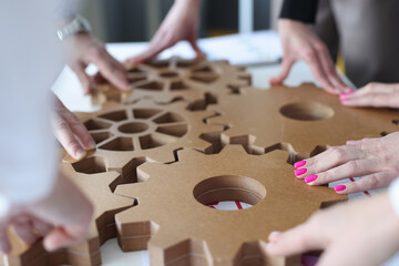 Employees connect together wooden gears on work table