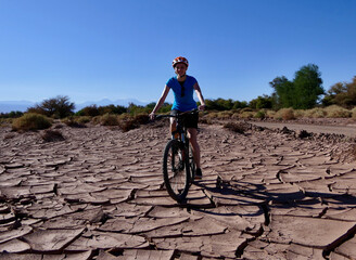 Active biker girl with helmet riding in dry desert before mountains and trees, Atacama salt desert, Chile