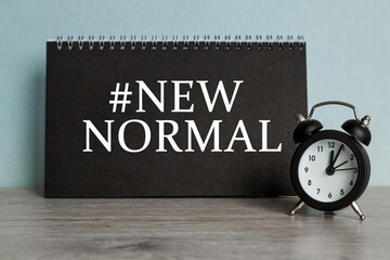 A word NEW NORMAL on black notebook with clock. Concept for time management and business.