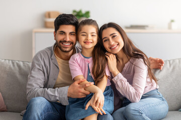 Family portrait. Excited arabic parents and cute little daughter posing together, embracing and...