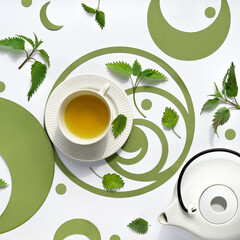 Nettle tea cup, stinging nettle herb leaves. Ornate flat lay, green paper Fibonacci sequence...