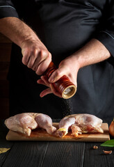 Chef or cook adds pepper to the chicken legs. Grill blank with raw chicken leg in the kitchen of a...