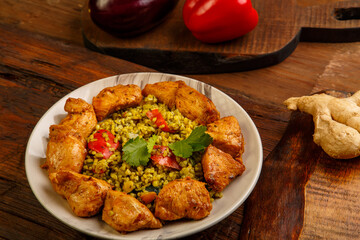 Food for suhoor in Ramadan bulgur post with beef in a plate on a wooden table next to vegetables on a board.