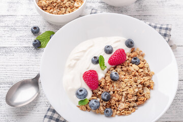Yogurt with baked granola and berries in white ceramic plate on wooden background. Healthy breakfast