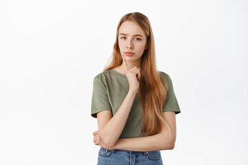 Suspicious young blond girl have doubts, thinking, looking serious and pensive at camera, making her decision, standing thoughtful against white background