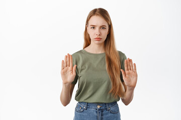 Fototapeta na wymiar Stop. Serious girl raising hands to block, say no, disapprove action and refusing something bad, frowning displeased, rejecting offer, standing against white background
