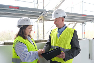 experienced elderly architect, female engineer constructor in protection of white helmet accept the object, sign documents at construction site, concept of civil engineering, cooperation