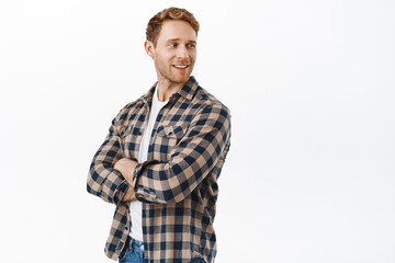 Handsome redhead man standing confident with crossed arms, turn head and looking aside at advertisement, smiling pleased while reading your logo on copyspace, standing over white background