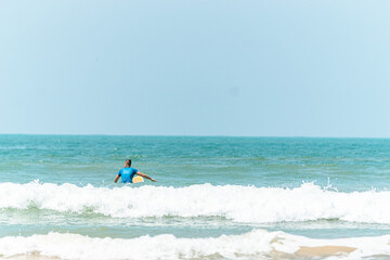 Fototapeta na wymiar Surfer z deską w wodzie, czekający na nadchodzącą fale, mężczyzna uprawiający sport wodny.