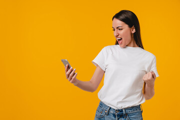 Happy as a winner excited young hispanic latin-american woman using smart phone isolated over...