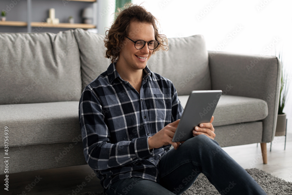 Poster happy millennial man using digital tablet browsing internet at home
