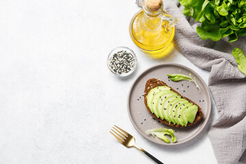 Whole grain rye bread toast with sliced avocado on white stone table background. Healthy avocado open sandwich for breakfast or lunch. Flat lay, top view, copy space