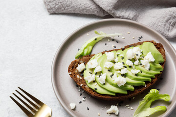 Whole grain rye bread toast with goat cheese and avocado on white stone table background. Healthy avocado open sandwich for breakfast or lunch. Flat lay, top view, copy space