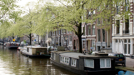 Fototapeta na wymiar Amsterdam, Netherlands, April 2011: A cityscape of canal with reflections and home boats with typical Dutch buildings in springtime.