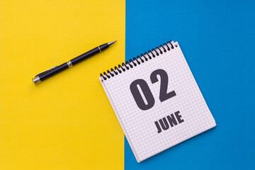 June 2nd. Day 2 of month, calendar date. Notebook with a spiral and pen lies on a yellow-blue background