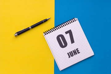 June 7th. Day 7 of month, calendar date. Notebook with a spiral and pen lies on a yellow-blue background