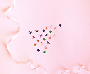 Shiny confetti of stars and round pieces on a pink background. Flat lay, top view. Decor with a thin pink ribbon. Festive background for your projects.