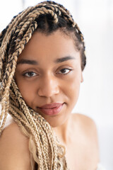 Charming african-american young woman with afro braids shirtless naked with clean soft smooth skin. Body and skin care, no makeup, natural beauty concept
