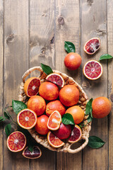 Composition of pile of blood oranges in a basket on a wooden table background. Flat lay, top view, copy space