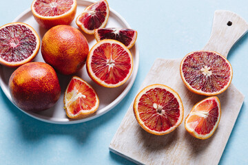 Composition of whole and sliced blood oranges in a plate on light blue table background. Flat lay, top view, copy space.