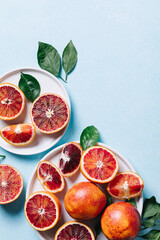 Composition of whole and sliced blood oranges in a plate on light blue table background. Flat lay, top view, copy space.